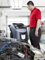 Automotive technician operating a Robinair A/C recovery and recharge machine in a professional repair shop, servicing a vehicle’s HVAC system with precision gauges and automated controls