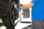Technician mounting an AC200-style wheel alignment clamp onto a vehicle wheel, securing the upper and lower arms to the rim
