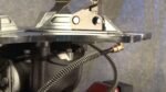 Close-up of a tire changer’s built-in bead sealing jet assembly, featuring the metal top plate, mounting hardware, and coiled air hose connected to a brass fitting