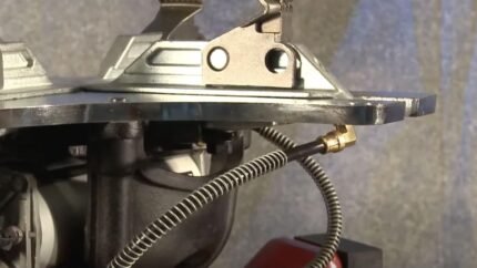 Close-up of a tire changer’s built-in bead sealing jet assembly, featuring the metal top plate, mounting hardware, and coiled air hose connected to a brass fitting