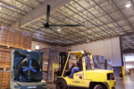 Cool Boss CB-20 HVLS 20-foot ceiling fan operating inside a busy warehouse with forklifts and stacked pallets, providing large-scale cooling and air circulation