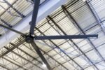 Close-up of the Cool Boss CB-24 HVLS fan installed in a steel beam warehouse ceiling, highlighting the Cool Boss logo and industrial mounting hardware