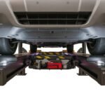 Undercarriage view of a vehicle on an alignment lift showing integrated center jack for lifting wheels during alignment and suspension service