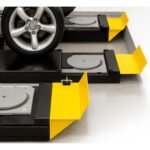 Close-up of vehicle wheels resting on alignment turnplates with integrated yellow wheel stops on four-post lift runways