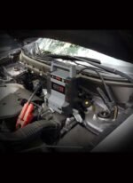 Schumacher DSR128 jump starter in use under the hood connected to a vehicle battery
