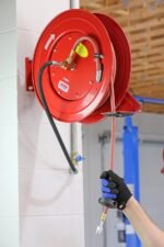 Lincoln 83754 Value Series hose reel mounted on a shop wall, demonstrating easy reach and professional installation for air-powered tools. Get it at Wrenchers.com