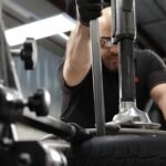 Technician using the Ranger R80EX tilt-back tire changer with dual assist towers for controlled mounting and demounting of low-profile and performance tires. Built for professional shops. SKU 5140139.