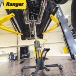 Ranger RTJ-1 transmission jack positioned under a raised vehicle on a two-post lift, supporting the drivetrain during service